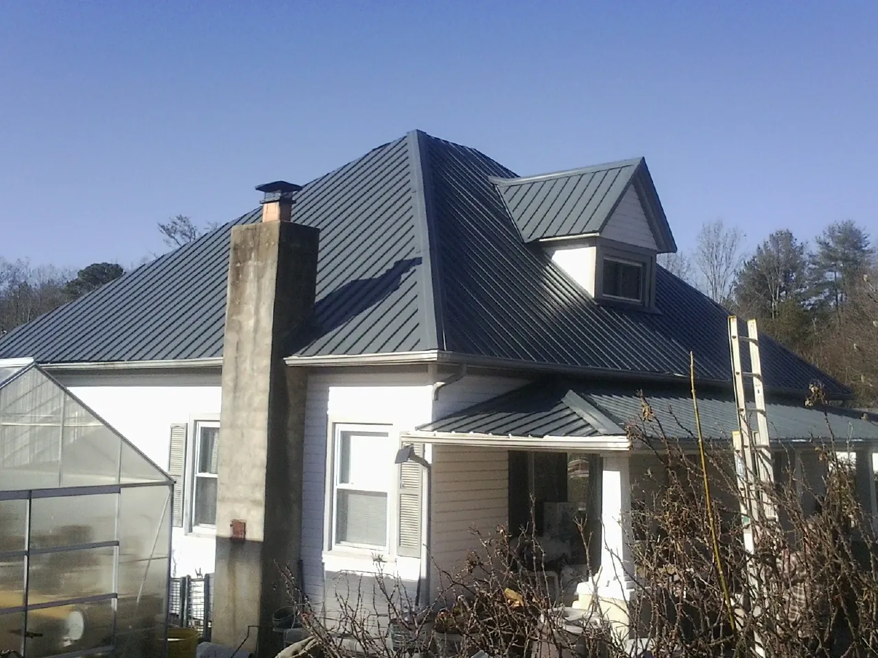 Dark blue standing seam metal roof on a white farmhouse with dormer — Slate & Tile Roof Repair by Roofing Brothers in Youngsville