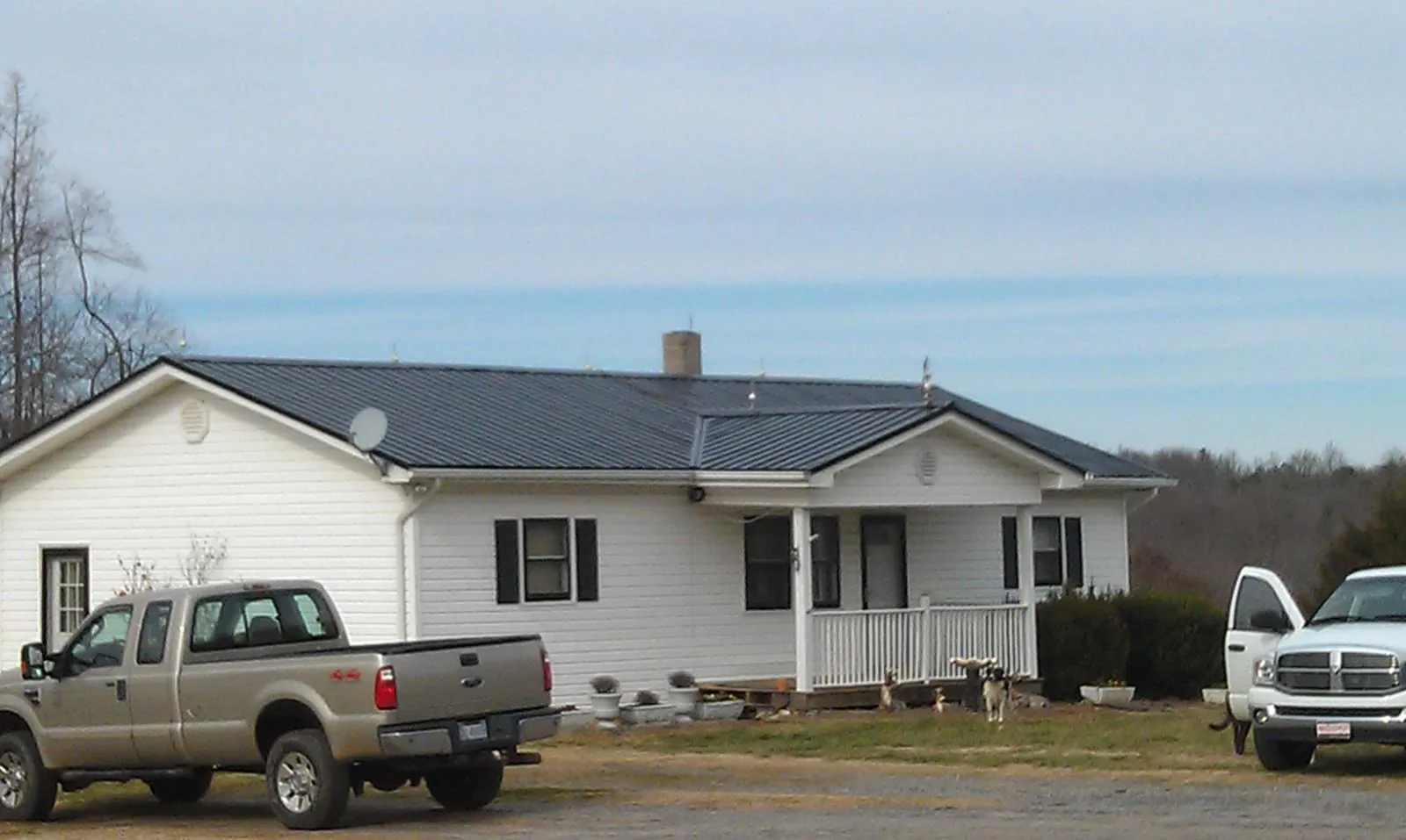 Finished dark metal roof on a white ranch home with work trucks parked in Youngsville