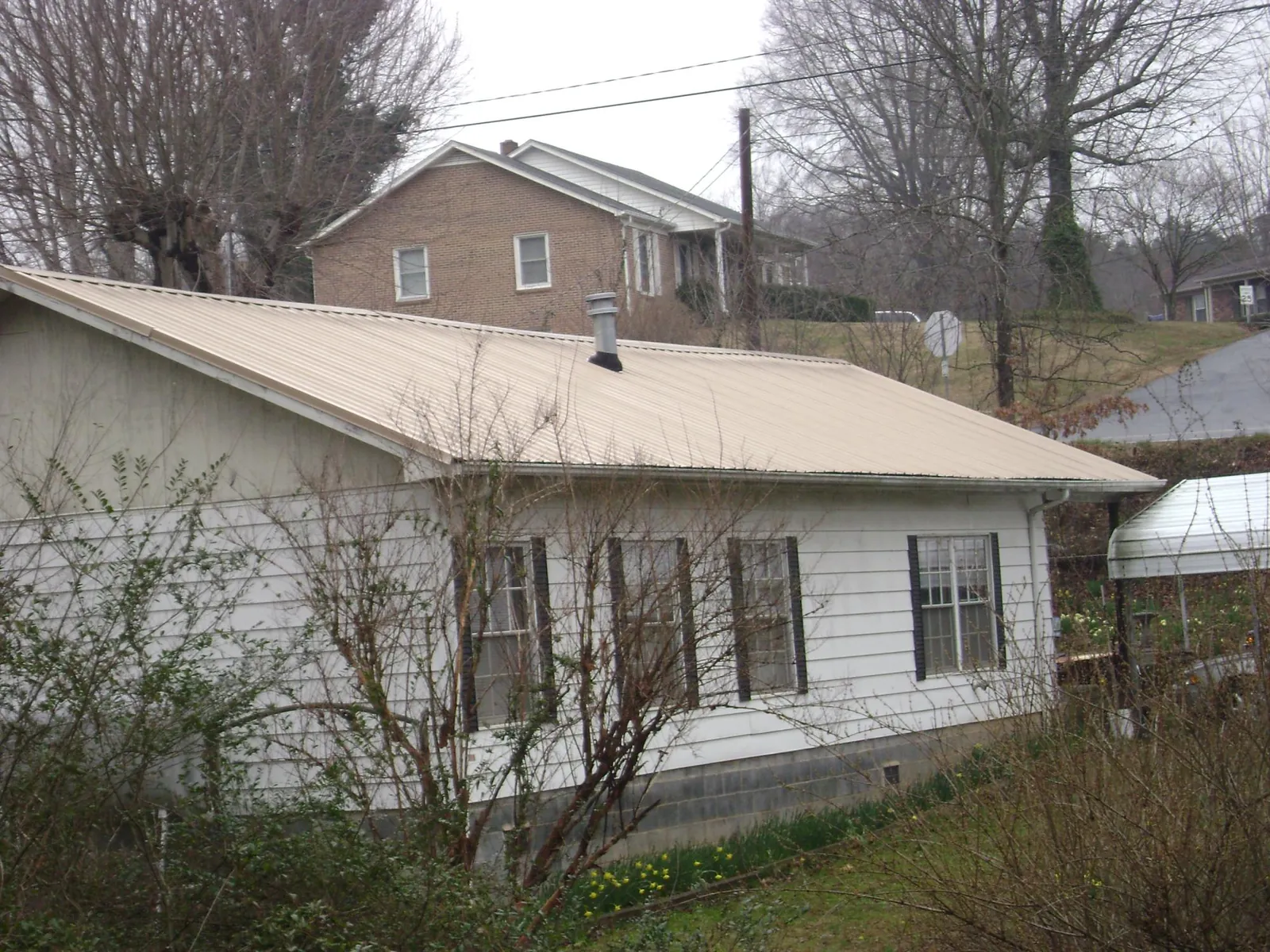 Tan metal roof on a white sided house set into a hillside — Commercial Roofing by Roofing Brothers in Youngsville