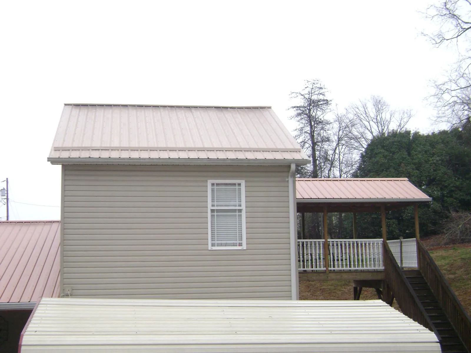 Tan metal roofs on a two story addition and attached porch, from a Roof Replacement job in Youngsville